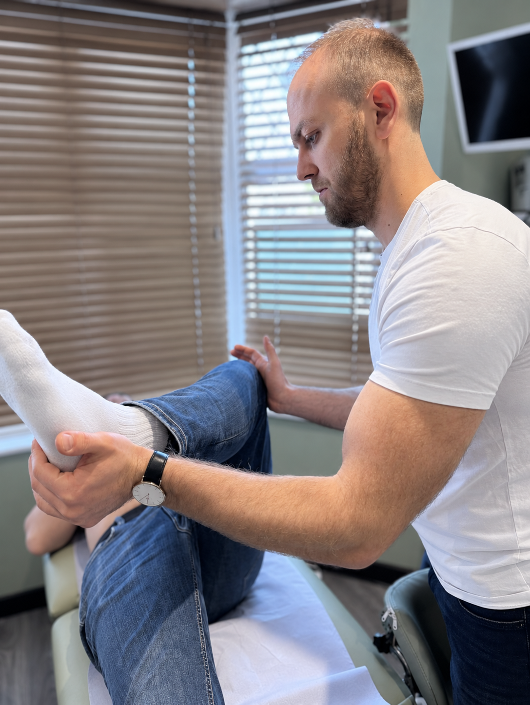 Physiotherapist supporting a patient’s bent leg during a lower limb assessment at Phoenix Medical Clinic in Watford.