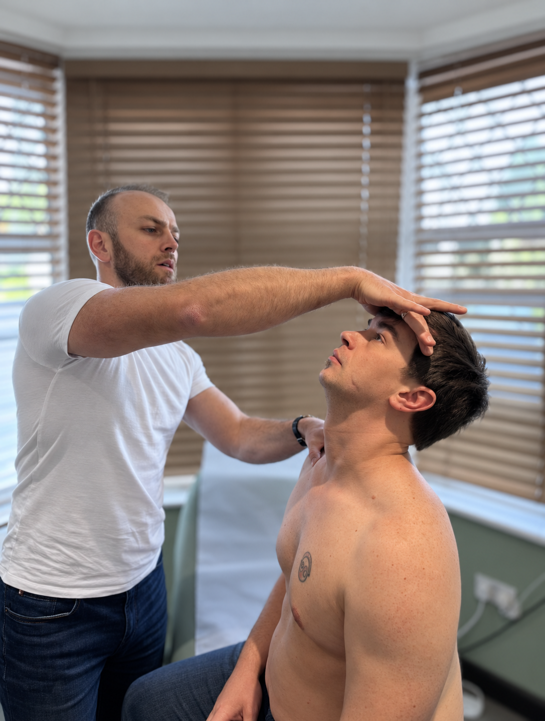 Physiotherapist assessing a seated patient’s neck movement at Phoenix Medical Clinic in Watford.